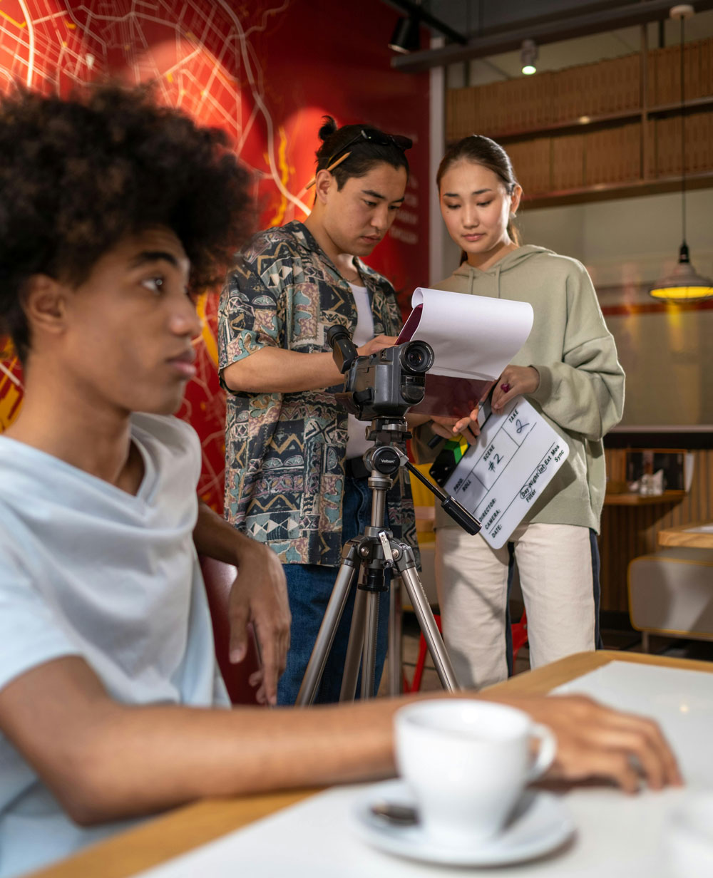 Een acteur op een stoel wacht terwijl een cameraman en iemand van productie aan het praten zijn.